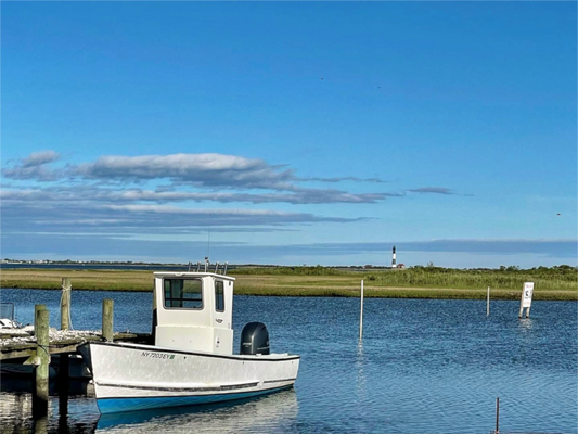 Boat on the Great South Bay with the Fire Island Lighthouse in the distance beneath an expansive coastal sk