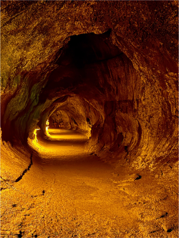 Illuminated lava tube beneath Kīlauea in Hawaiʻi Volcanoes National Park on the Big Island, with warm amber light revealing the volcanic rock walls.